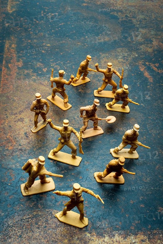 Small toy soldiers are positioned in a playful arrangement on a rough surface. Their poses suggest movement and action, inviting creative scenarios for playtime or collection