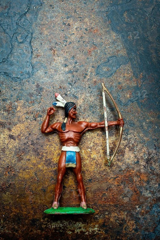 A bright plastic toy archer stands poised with his bow drawn back, showcasing the figure of an Indian Native American