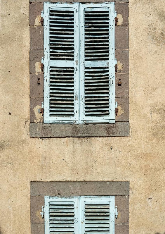 Two sets of vintage blue shutters add charm to a weathered wall, showcasing the beauty of rustic architecture and evoking a sense of history and character. France