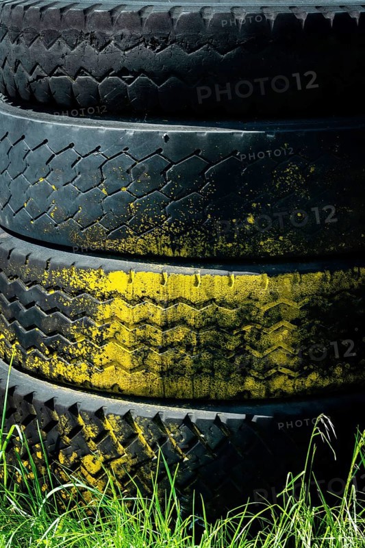 Tires are stacked on top of each other, featuring a vibrant yellow band. The background consists of lush green grass, illuminated by sunlight, creating a striking contrast