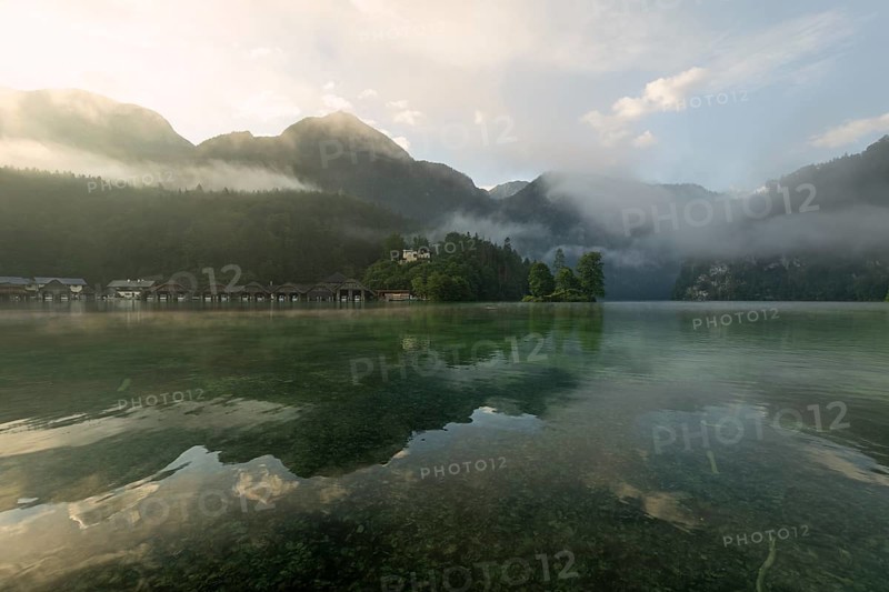 Mystical morning at Königssee in Schönau with boathouses and Christlieger. Sunrise and beautiful wafts of mist over the Königssee in the basin