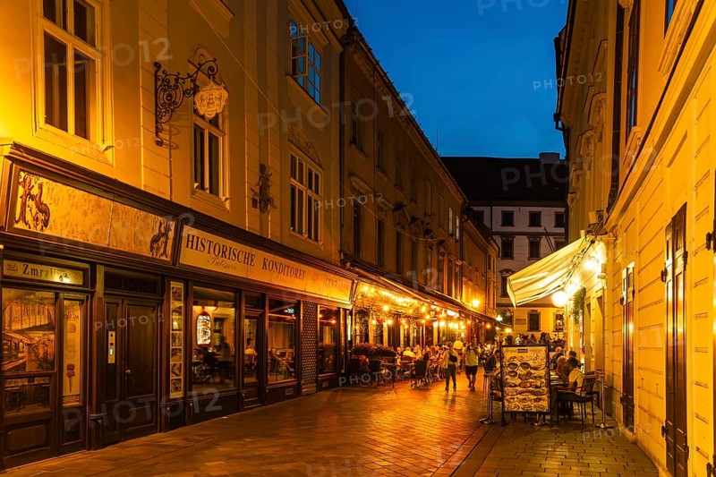 Cosy alley in the old town with illuminated cafés and historic pastry shop in Bratislava, Slovakia