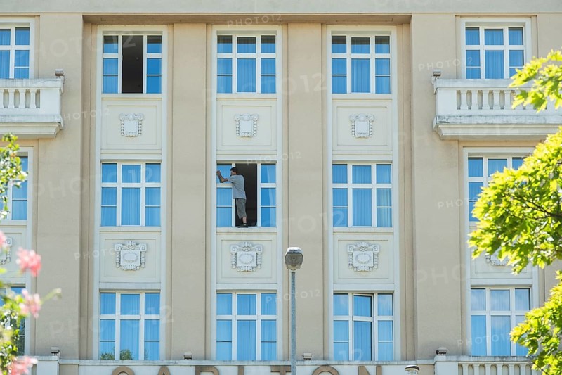 A window cleaner cleans a window and stands on the windowsill, Bratislava, Slovakia
