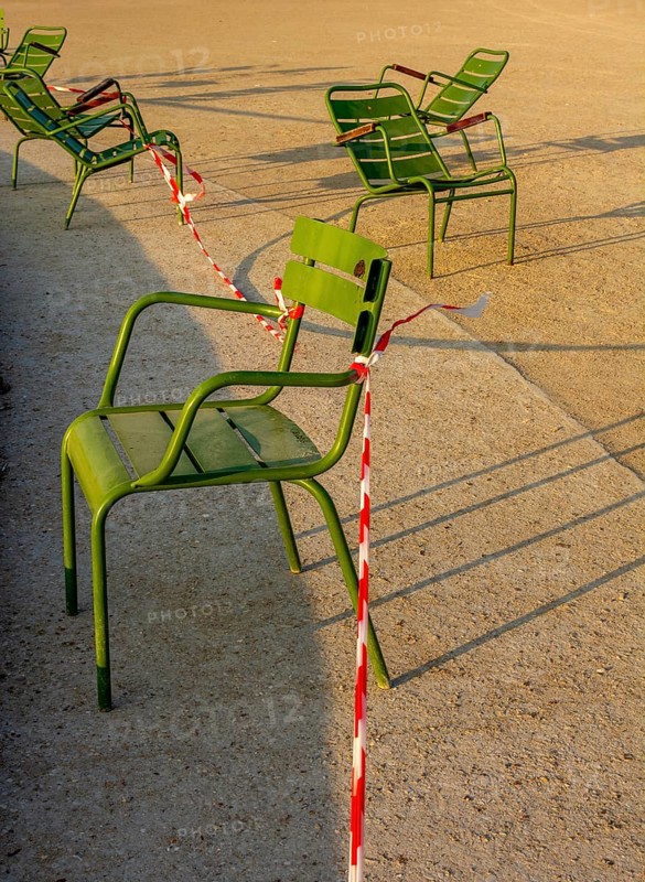 Several green chairs are placed next to each other in the sun at Tuileries Garden. Red and white caution tape surrounds one chair, indicating some areas may be restricted for visitors. Paris. France