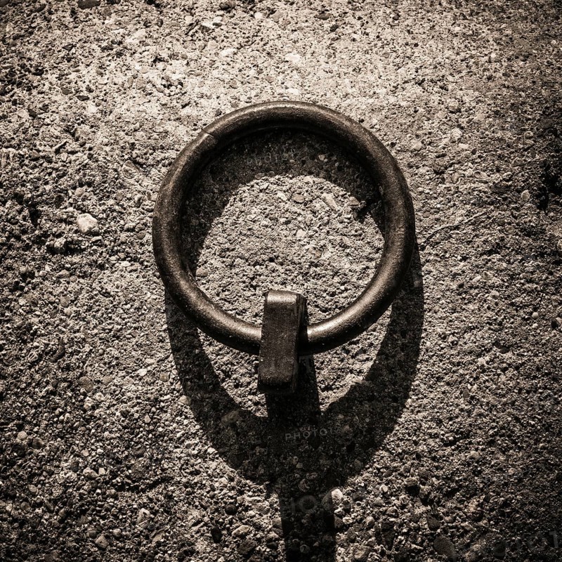 Mooring rings made of iron are embedded in the dockside, showcasing a rugged texture under soft twilight light. Shadows stretch across the concrete, enhancing the industrial aesthetic