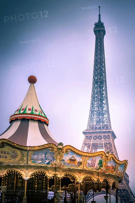 A vintage carousel spins joyfully in a park, with the Eiffel Tower towering majestically in the background. Visitors enjoy a delightful day in scenic Paris, surrounded by beauty. France