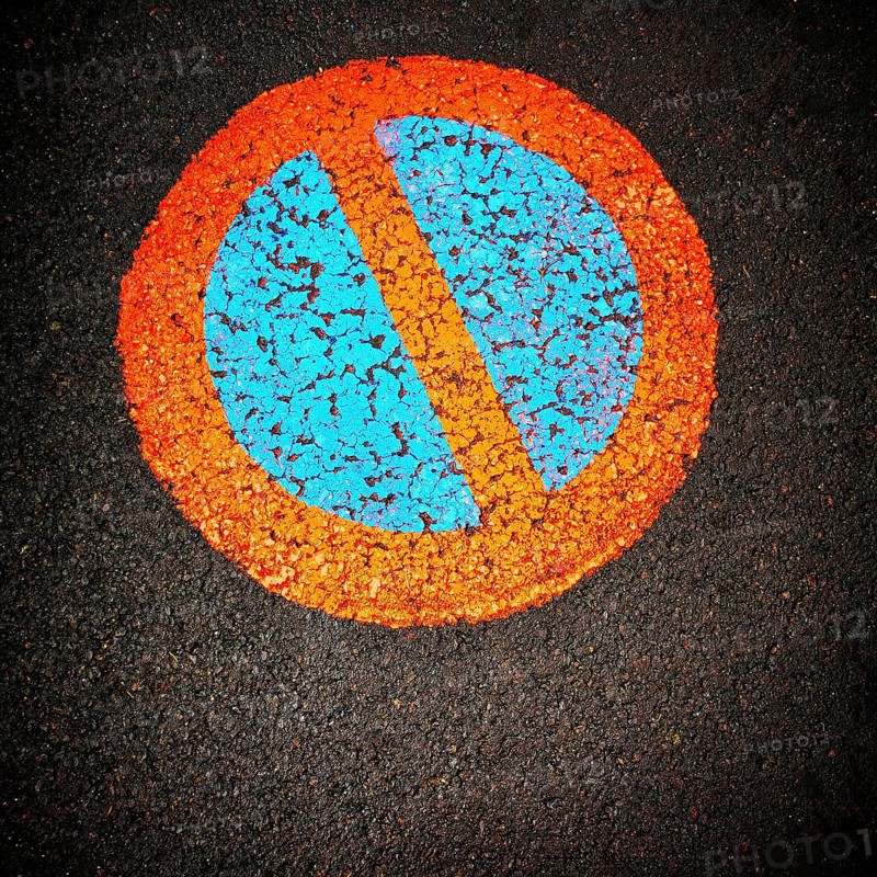 A vibrant no parking symbol is prominently displayed on a black asphalt surface, featuring a blue circle intersected by an orange diagonal line, creating a striking visual contrast