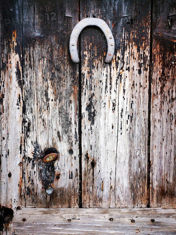 A rustic wooden door features a weathered texture, complete with a vintage horseshoe mounted at the top. The door's grain showcases years of wear, adding character and charm. Puy de Dome. Auvergne Rhone Alpes. France