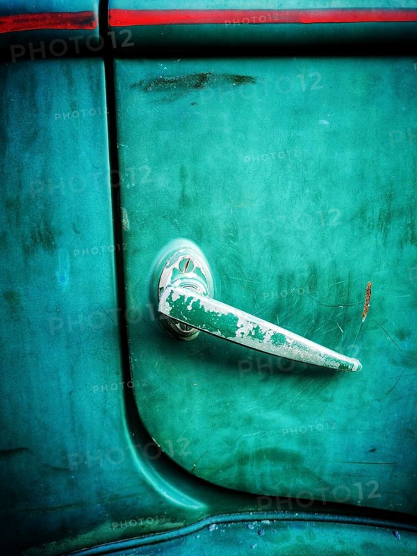 A close-up view of a vintage car door handle featuring a weathered surface and vibrant green paint. This detail showcases the charm of classic automobiles found outdoors