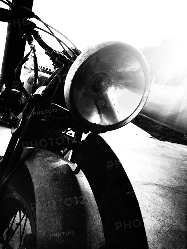 A detailed close-up captures the headlight of an antique motorcycle, highlighting its vintage design and reflecting the surrounding environment in black and white