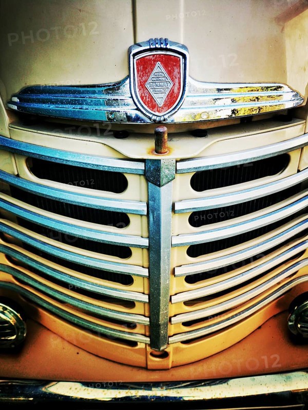 The front grille of a vintage truck features intricate chrome detailing with a prominent emblem. The weathered appearance reflects years of use and automotive design history