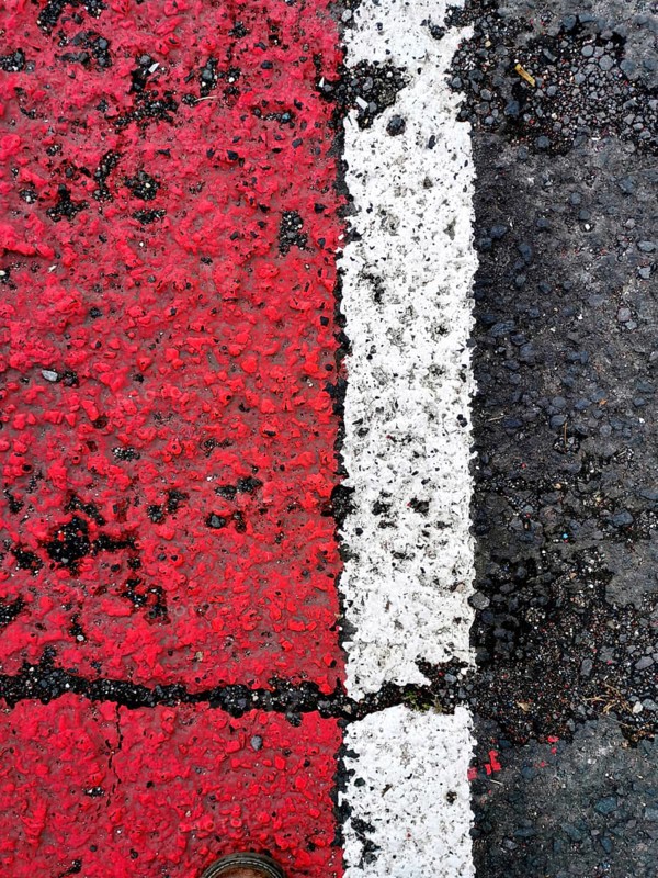 Bright red and white lines mark the asphalt surface, showcasing a clear division. A shoe is positioned close to the lines, adding perspective and detail to the scene
