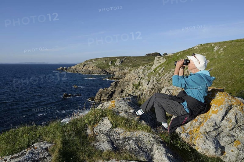 Woman with binoculars on the cliffs, Cap Sizun, Finistere department, Brittany, France