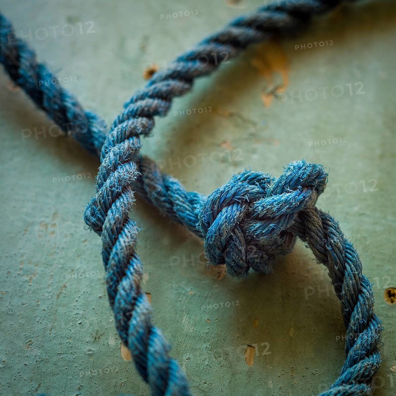 A close-up view reveals an intricately tied blue rope knot resting on a textured surface, highlighting the detailed craftsmanship involved in knot-making