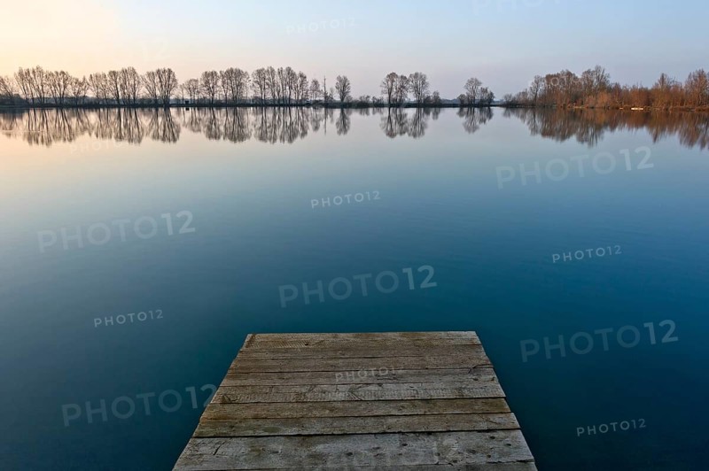 Sunset at Moosinninger Weiher with wooden footbridge, quarry pond, fishing pond for carp, reflection of the trees on the shore, smooth calm water, Moosinning in Erdinger moss, Erding, Upper Bavaria, Bavaria, Germany