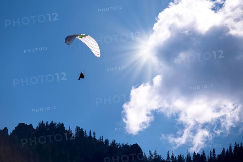 A paraglider flies under a bright sun and clouds in the blue sky, Bavaria, Germany