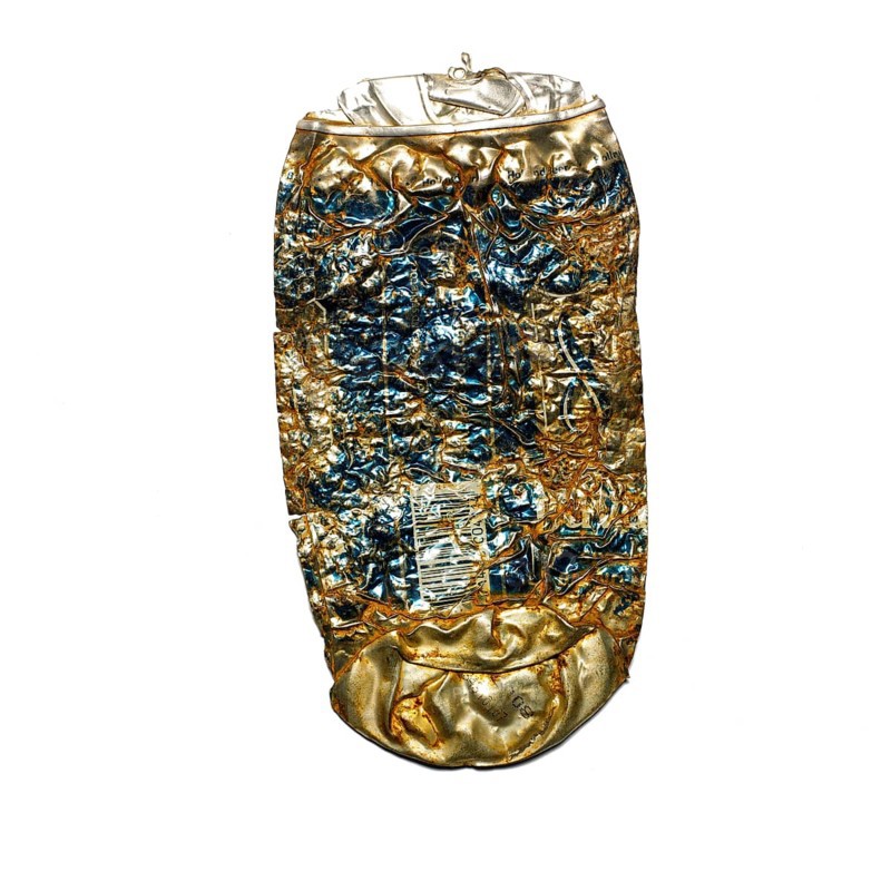 A crushed beer can rests on a city sidewalk, highlighting issues of litter and pollution. Its worn surface shows signs of weathering, reflecting the impact of human activity on the environment