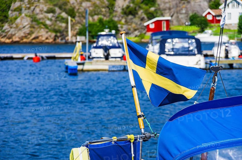 The Swedish flag flies at the stern of a boat in the marina of Henan on Orust, Bohuslän, Västra Götalands län, Sweden