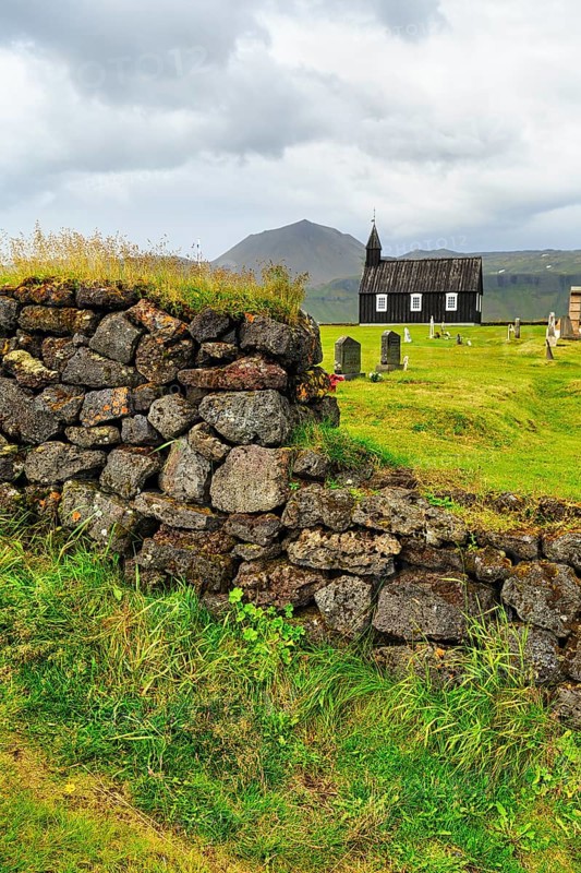Traditional black church with cemetery, view through a stone wall to the wooden church Budakirkja, Búðir, Budir, Snaefellsnes Peninsula, Iceland