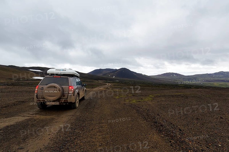 Off-road vehicle, SUV with roof tent driving on gravel track, barren volcanic landscape with snow fields, mountain peaks with rain clouds, Snaefellsjökull, Snæfellsnes peninsula, Snaefellsnes, West Iceland, Iceland