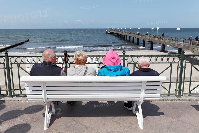 Holidaymakers sitting on a bench on the beach promenade, one is wearing strikingly colourful clothes, Baltic resort Kühlungsborn, Baltic Sea, Mecklenburg-Western Pomerania, Germany