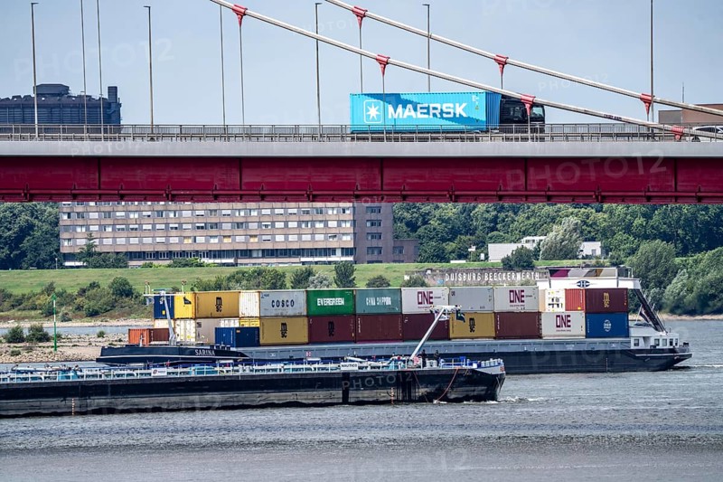 Barges on the Rhine at Ruhrort harbour, container freighter on uphill journey, Friedrich-Ebert-Bridge, road bridge over the Rhine between Homberg and Ruhrort, Maersk container on lorry on the bridge, Duisburg, North Rhine-Westphalia, Germany