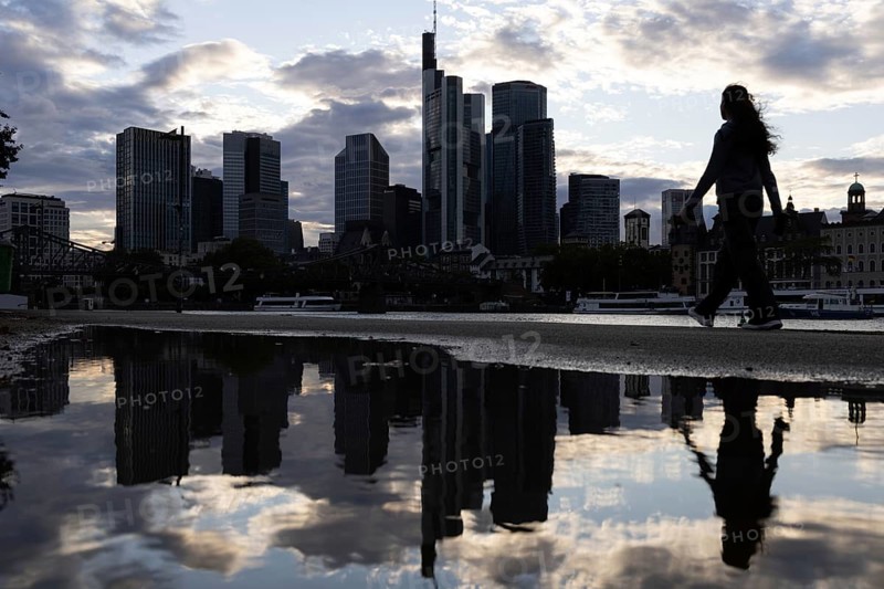 A woman walks along the banks of the Main in the rain in front of the Frankfurt banking skyline, Frankfurt am Main, Hesse, Germany