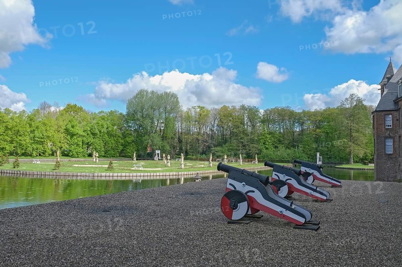 Small cannons at the edge of a park with a pond and sculptures, under a blue sky with clouds, moated castle Anholt, Münsterland, North Rhine-Westphalia, Germany