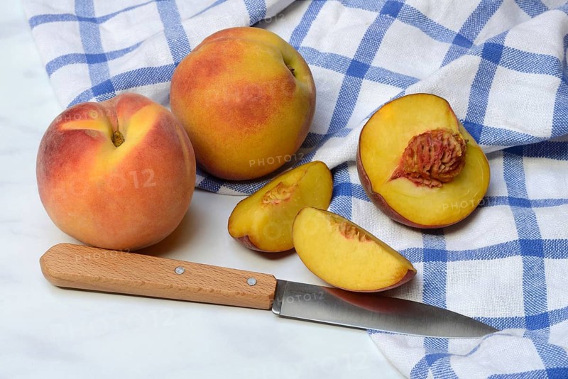 Peach with knife on kitchen towel, peach halves, Prunus persica
