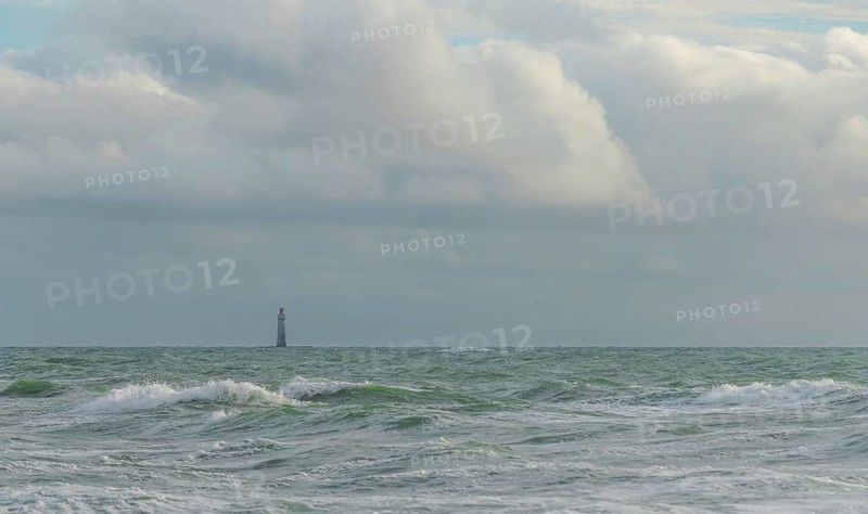 Waves crash against the shore while a lone lighthouse looms in the distance under a sky filled with dramatic clouds. The setting captures the calm yet powerful essence of the sea. Les Sables d'Olonne, Vendee, France
