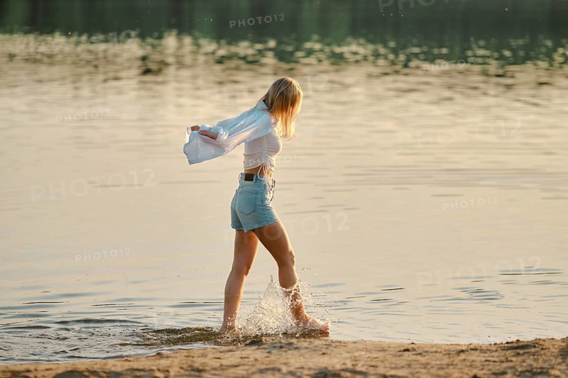 A young woman strolls through shallow water at a peaceful lakeshore creating splashes with her feet during sunset