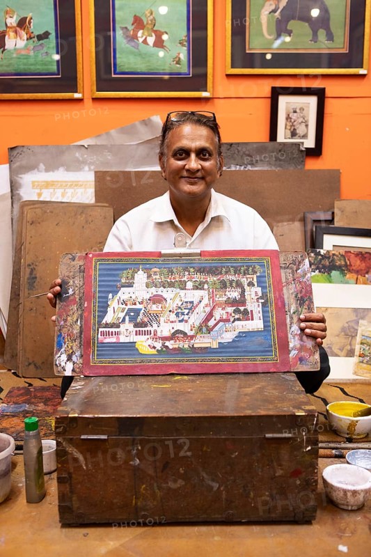 Miniature painter, 50 years old, shows a picture of the royal city palace in his studio, Udaipur, Rajasthan, India