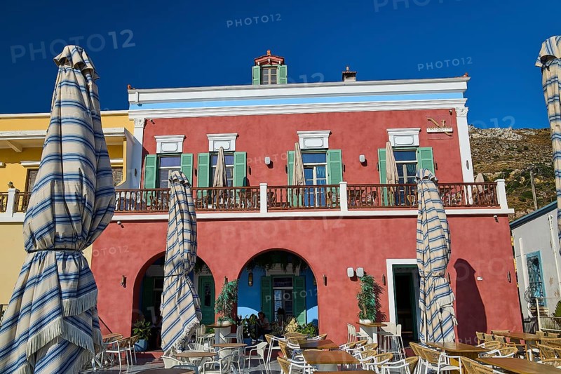 Building with red façade and terrace café under striped parasols, Agia Marina, Leros, Dodecanese, Greek Islands, Greece