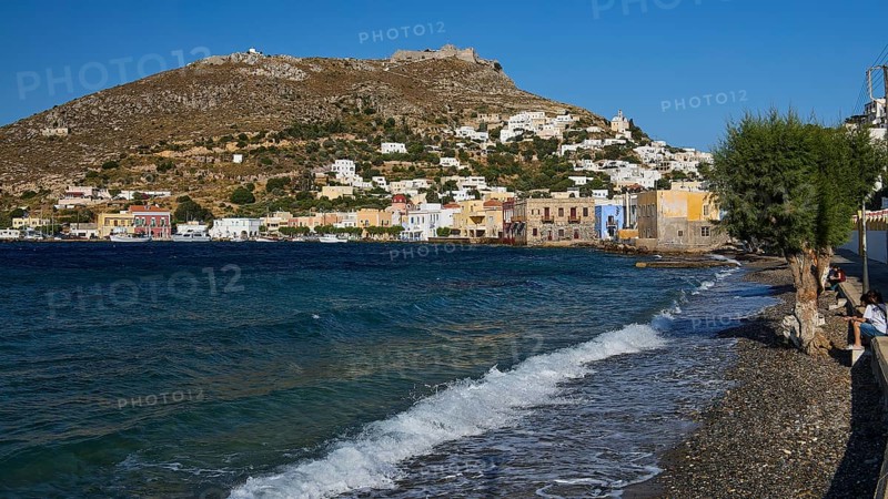 Panteli fortress, beach with pebbles, wavy sea, coast with colourful buildings and hills in the background, Agia Marina, Leros, Dodecanese, Greek Islands, Greece