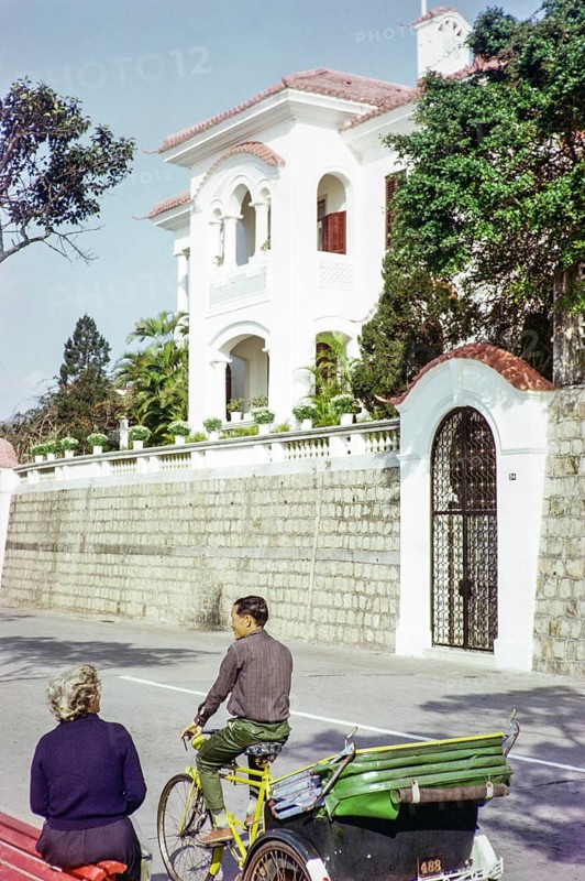 Tricycle rickshaw rider outside Portuguese colonial villa building, Avenida da Republica, Macau, Asia 1964