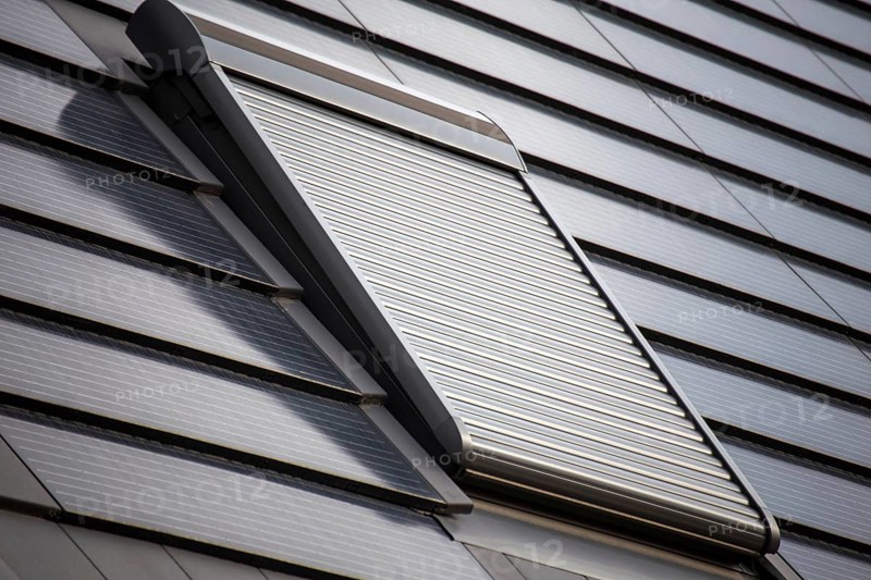 Roof window with roller shutter on a roof covered with solar tiles