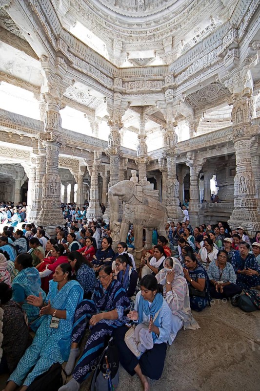 Indian woman pray between the white marble pillars around a marble elephant statue in the Adinath temple in Ranakpur, Jain temple, Rajasthan, India