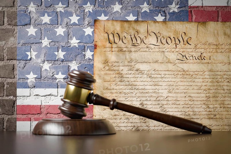 United states constitution and american flag on wall with gavel resting on table in front