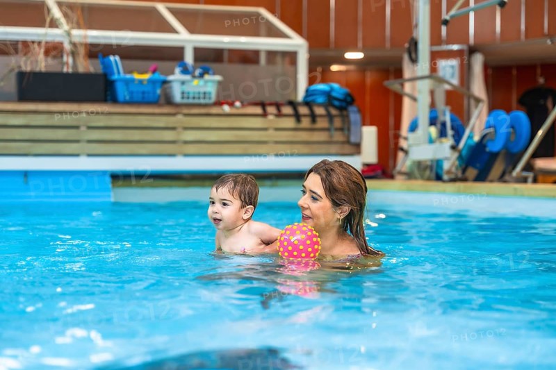 Mother and son having fun together playing with a colorful inflatable ball during a swimming lesson in an indoor pool