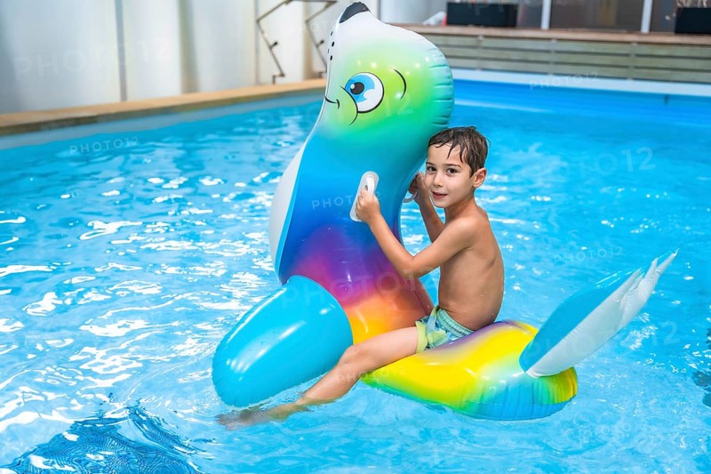 Boy enjoying summer holidays while riding an inflatable toy in a vibrant blue swimming pool, embracing the joy of childhood fun