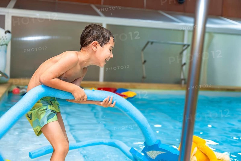 Happy boy playing with a pool noodle in an indoor swimming pool, relishing a fun summer activity while enjoying the water and sunshine