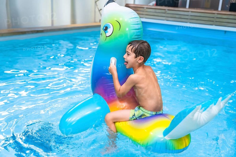 Happy child enjoying playful moments with a colorful inflatable seal in a sparkling pool during sunny summer holidays