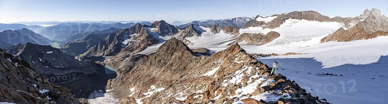 Mountaineer on a rocky ridge on the Wilder Freiger mountain peak, behind signal peak and Becher peak with Becherhaus, picturesque high mountain landscape, view of Übeltalferner glacier and rocky mountain peaks Königshofspitz and Sonklarspitze, Stubai Alps, South Tyrol, Italy