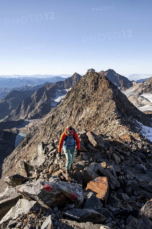 Mountaineer on a rocky ridge, ascent to the Wilder Freiger mountain peak, behind her the summit of the Becher with Becherhaus, picturesque high mountain landscape, Stubai Alps, South Tyrol, Italy