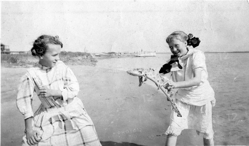 Two girls on the beach playing with a catshark, ca. 1930, location unknown
