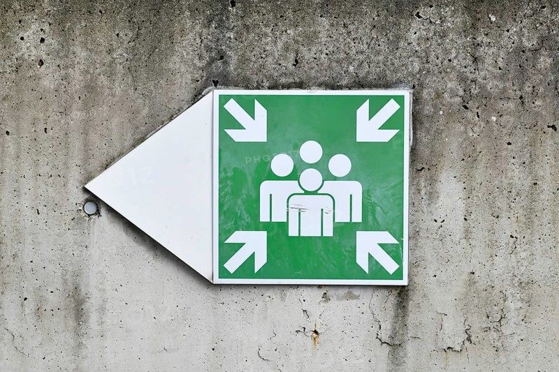 Emergency assembly point sign on concrete wall. Indicates designated safe meeting area for evacuation or disaster situations