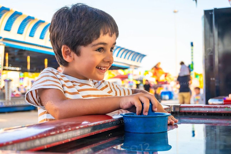 Smiling young boy playing a game at an amusement park, surrounded by colorful attractions and bright lights, capturing the essence of childhood fun