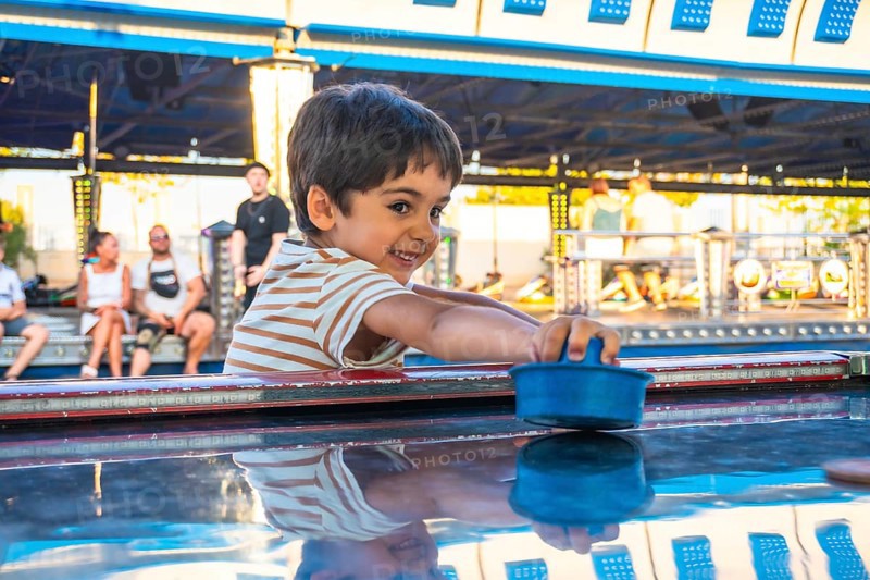 Smiling boy playing air hockey at an amusement park, surrounded by colorful lights and people, capturing the joy of childhood fun