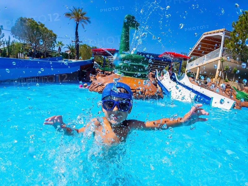 Happy child wearing blue baseball cap and swimming goggles, playing and splashing in a pool during summer holidays