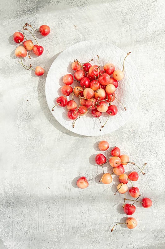 Yellow cherries on a white platter, scattered on the table, natural light, top view